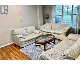A living room with a beige couch, a glass coffee table, and a rug.