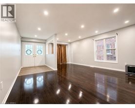 A spacious room with wood flooring and a large window with a view of a brick building.