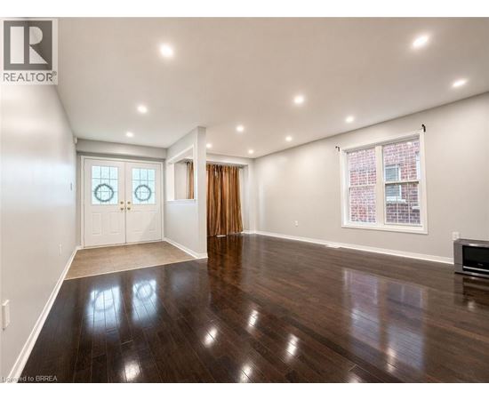 A spacious room with wood flooring and a large window with a view of a brick building.