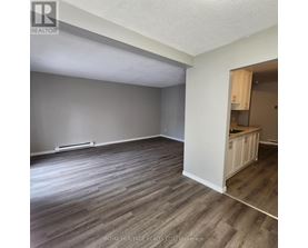 A room with wooden flooring and a kitchenette in the corner.
