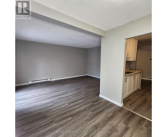 A room with wooden flooring and a kitchenette in the corner.