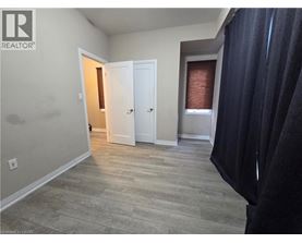A room with a doorway leading to another room, a window with blinds, and a curtain on the right side.