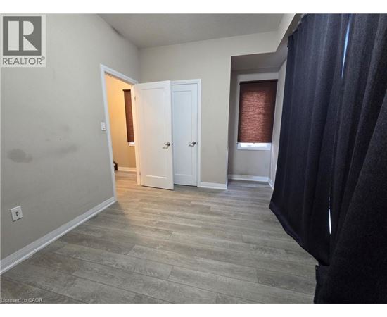 A room with a doorway leading to another room, a window with blinds, and a curtain on the right side.