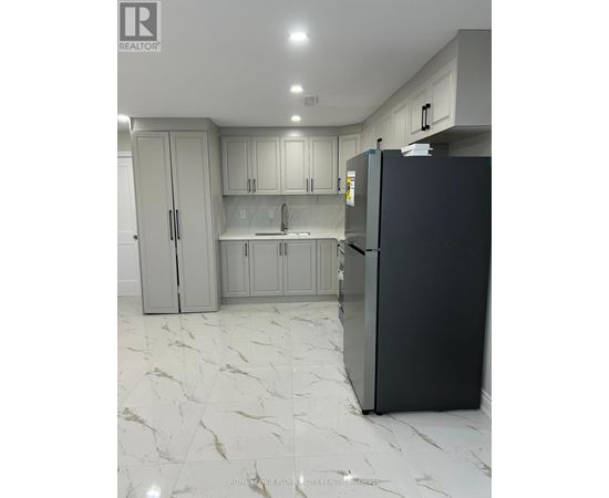 A black refrigerator in a kitchen with marble flooring and white cabinets.