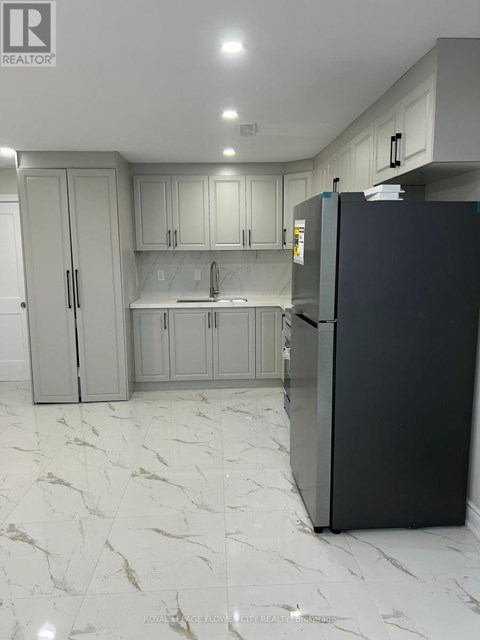 A black refrigerator in a kitchen with marble flooring and white cabinets.