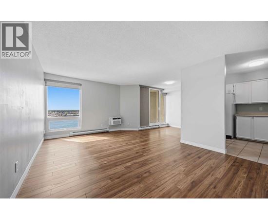 A spacious room with wooden flooring and a large window overlooking the beach.