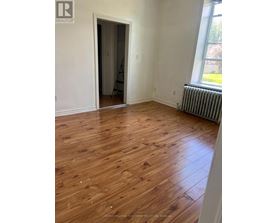 A room with wooden flooring and a window with a view of a lawn.