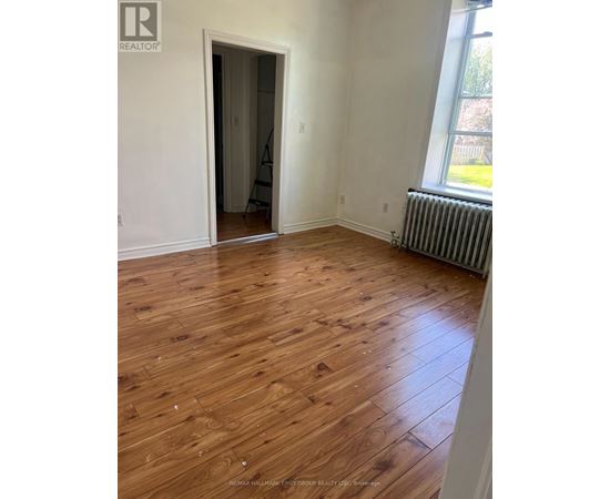 A room with wooden flooring and a window with a view of a lawn.