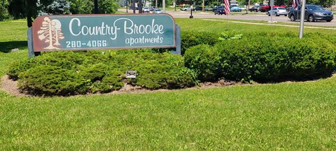 A sign for Country Brookes Apartments is surrounded by green bushes.