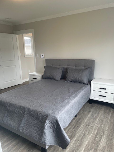 A bed with a grey comforter and two pillows sits in a room with a white door and a white nightstand.