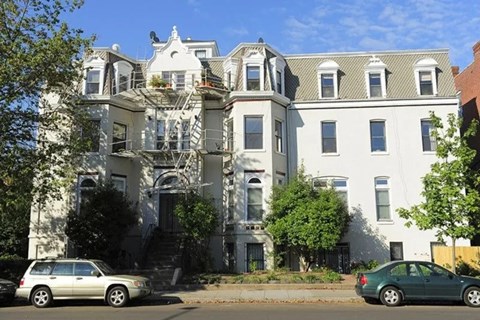 A white building with a grey roof and a green car parked in front.