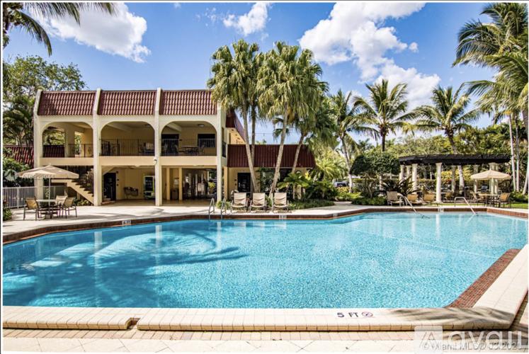 A large swimming pool is surrounded by palm trees and a building with a covered patio.
