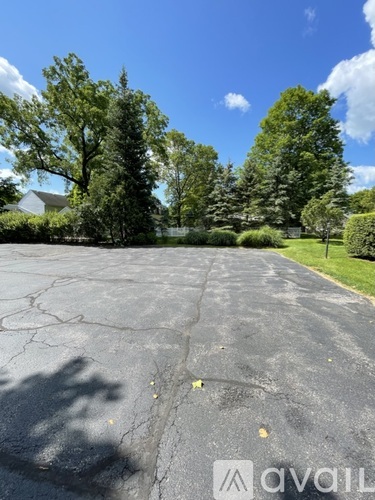 A large, cracked parking lot with trees and a house in the background.