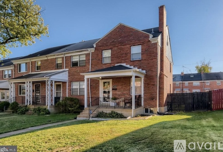 A brick house with a porch and a tree in front.