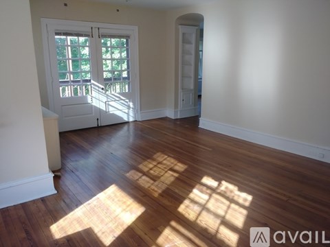 A room with wooden floors and a large window with sunlight shining through.