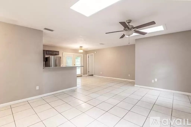 A spacious room with a ceiling fan and a refrigerator in the corner.