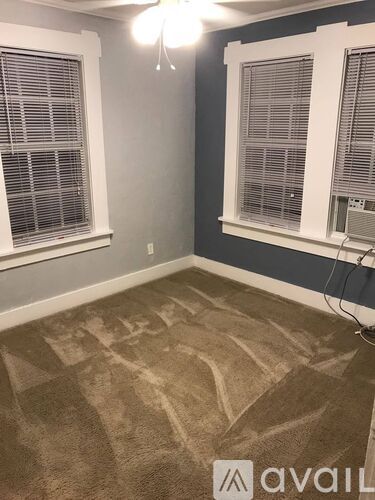 A room with a carpet and two windows with blinds.