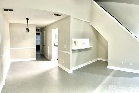 A spacious room with a staircase on the right and a doorway leading to another room.