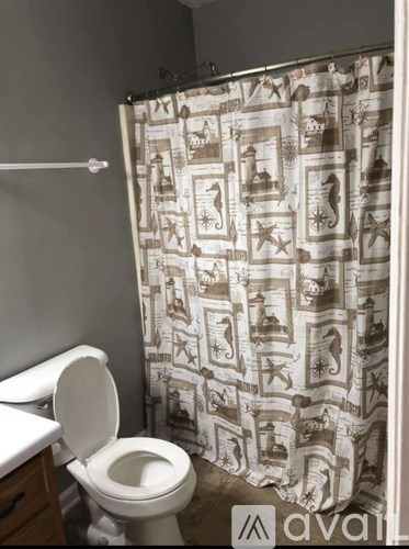 A toilet with a shower curtain with a pattern of houses and trees.