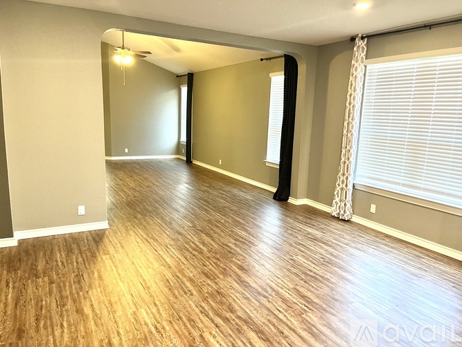A spacious room with wooden flooring and a window with blinds.