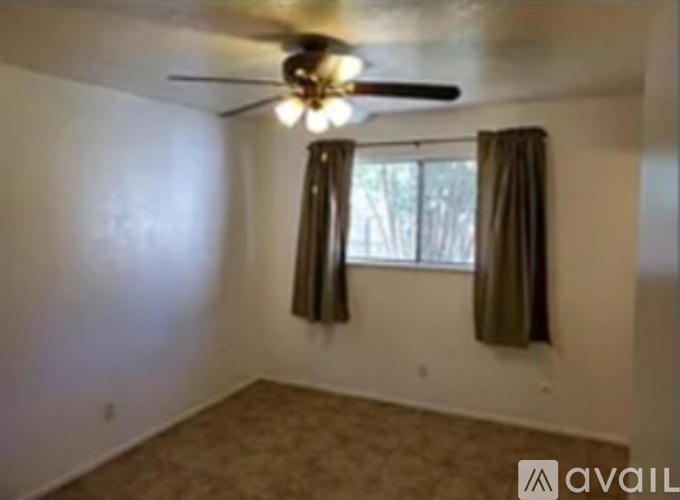 A room with a ceiling fan and a window with curtains.