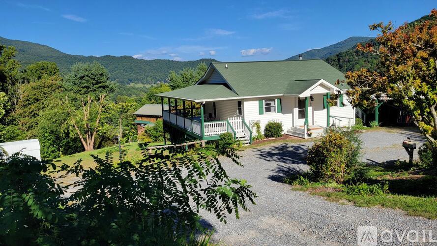 A house with a green roof is surrounded by trees and mountains.