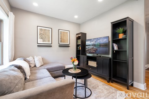 A living room with a grey couch, a black cabinet, and a small table with a vase of flowers on it.