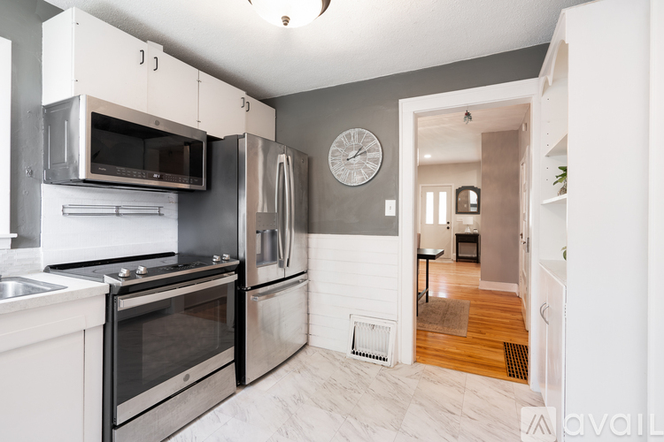 A kitchen with a white oven and microwave, a clock on the wall, and a doorway leading to another room.