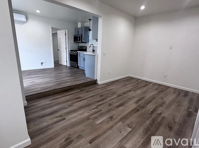 A room with wooden flooring and a kitchen area in the background.