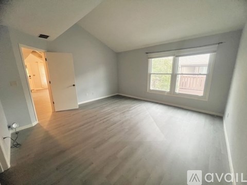 A spacious empty room with wooden flooring and a window.