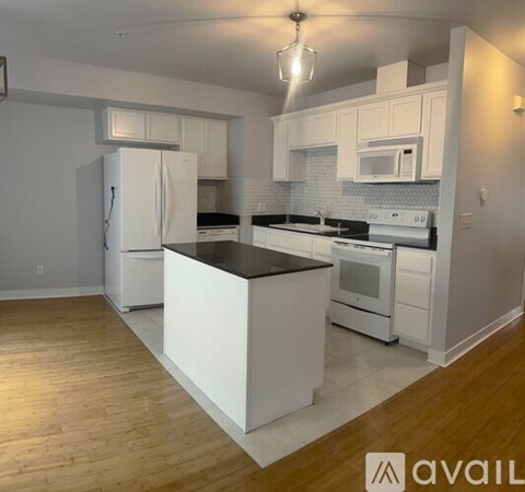 A kitchen with white cabinets and appliances, a black countertop, and wooden flooring.