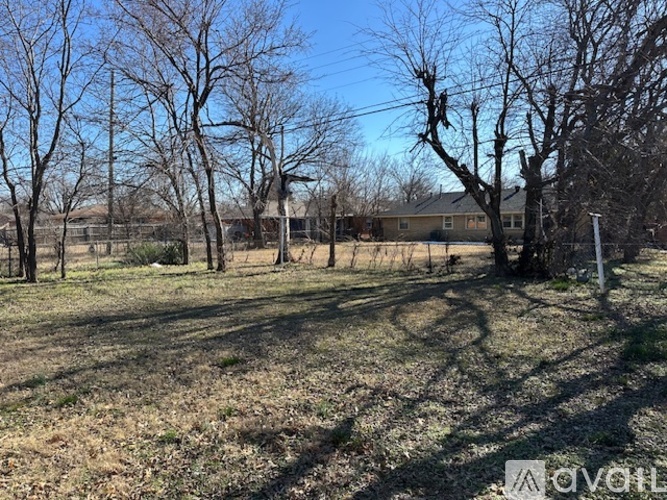 A field with trees and a house in the background.