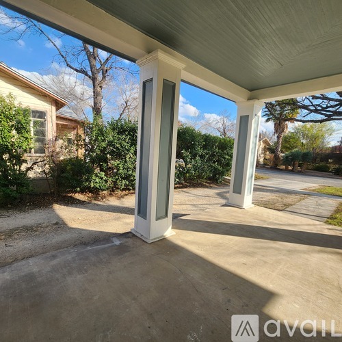 A porch with a white column and a view of a house and trees.