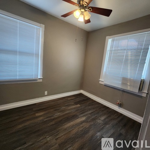 A room with a ceiling fan and two windows.