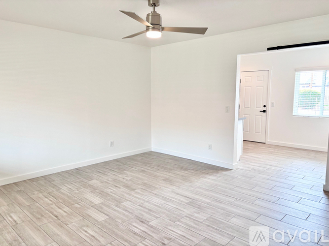 A spacious room with a ceiling fan and light, hardwood flooring, and a door leading to another room.