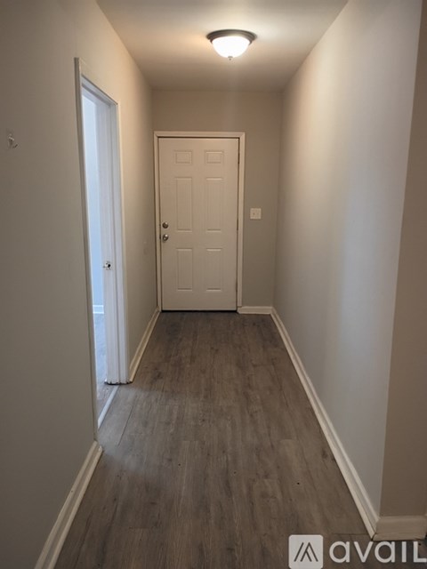 A hallway with a white door and wooden flooring.