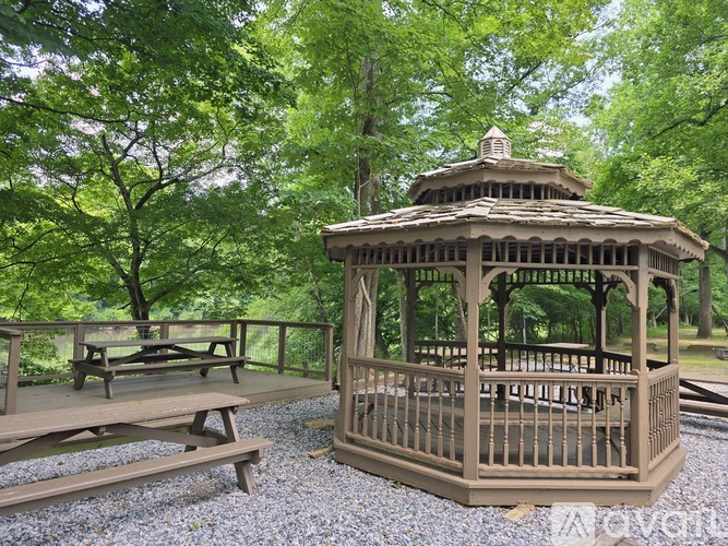 A gazebo is surrounded by trees and has picnic tables.