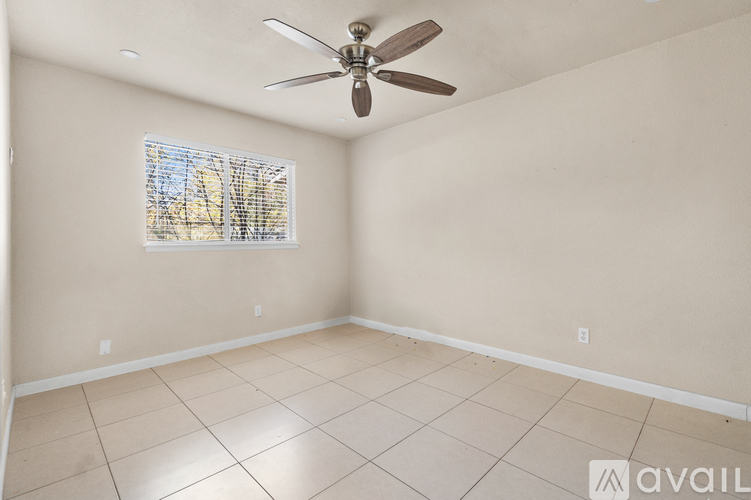 A room with a ceiling fan and a window with a view of trees.