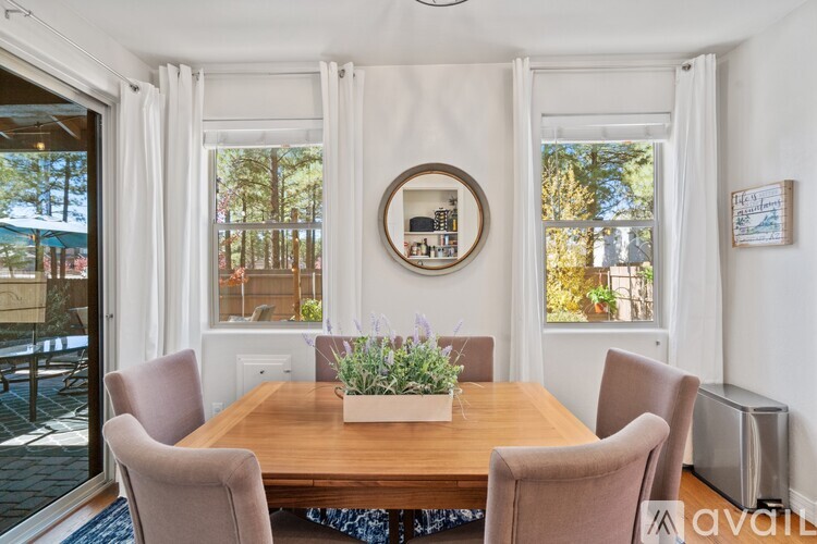 A dining room with a wooden table and chairs, a round mirror, and a window with curtains.