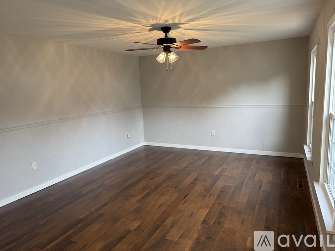 A room with wooden floors and a ceiling fan with a light bulb.