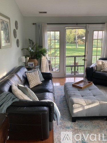 A living room with a black leather couch and a grey ottoman.