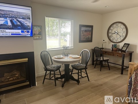 A living room with a fireplace, a dining table set for two, and a television playing news.