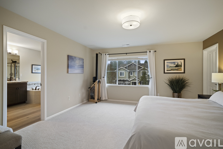 A bedroom with a large bed and a window with a view of a house.