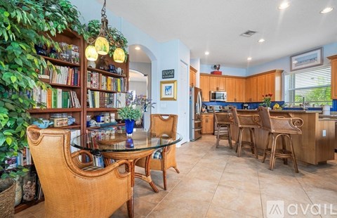 A living room with a glass table and chairs, a bookshelf, and a dining area with a kitchen in the background.