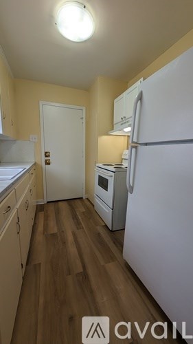 A kitchen with a white fridge and wooden floors.