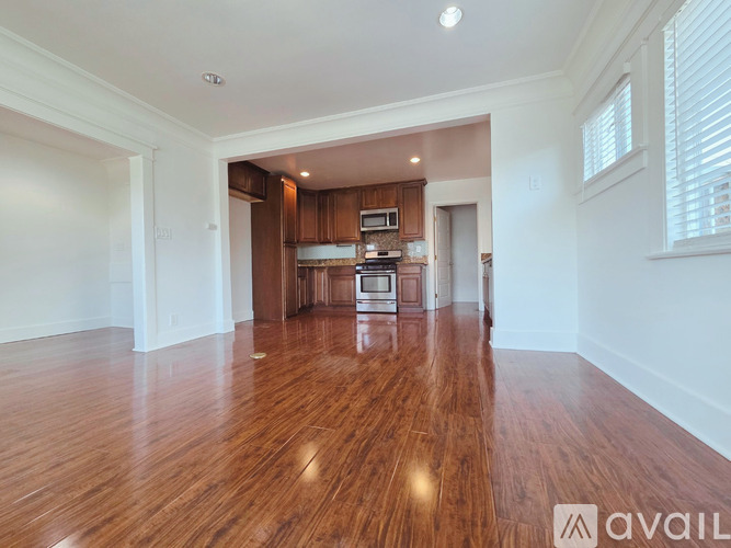 A spacious room with wooden floors and a kitchen area in the background.