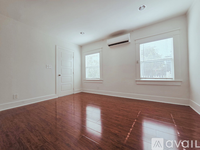 A room with wooden flooring and two windows with blinds.