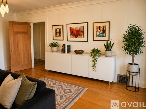 A living room with a black couch and a white cabinet with plants on top.