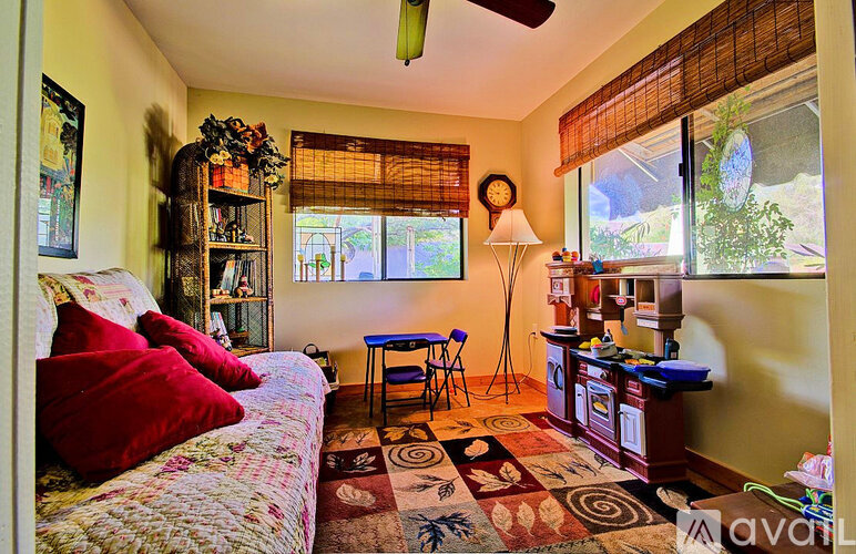 A living room with a sofa, a table, a fan, and a window with blinds.