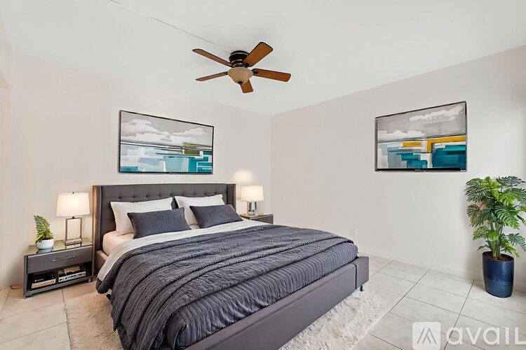 A bedroom with a large bed, a ceiling fan, and two framed pictures on the wall.